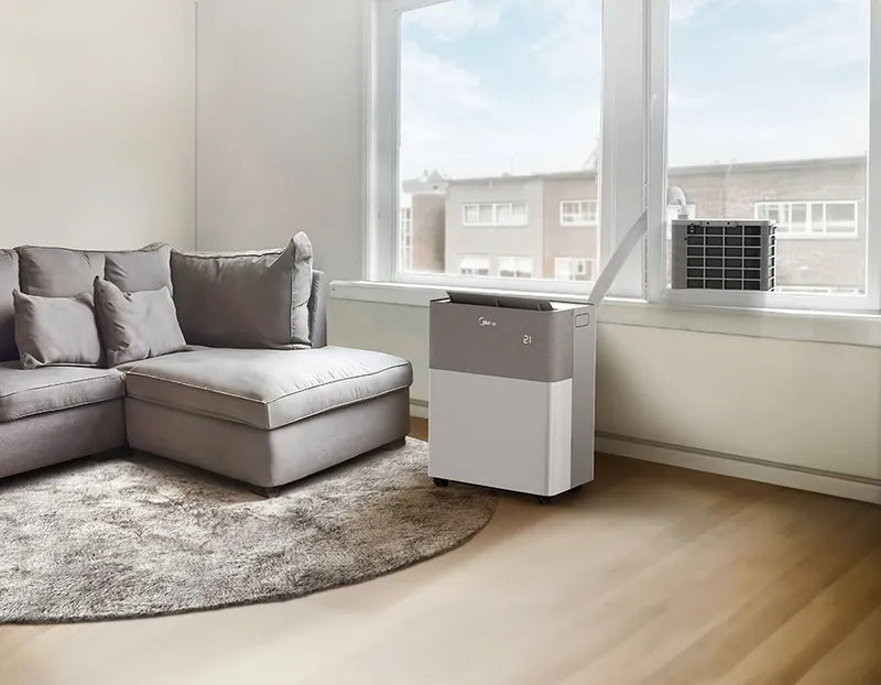 Innengerät der Midea PortaSplit im Wohnraum, daneben hängt das Außengerät im gekippten Fenster, verbunden über den flachen weissen Kältemittelschlauch