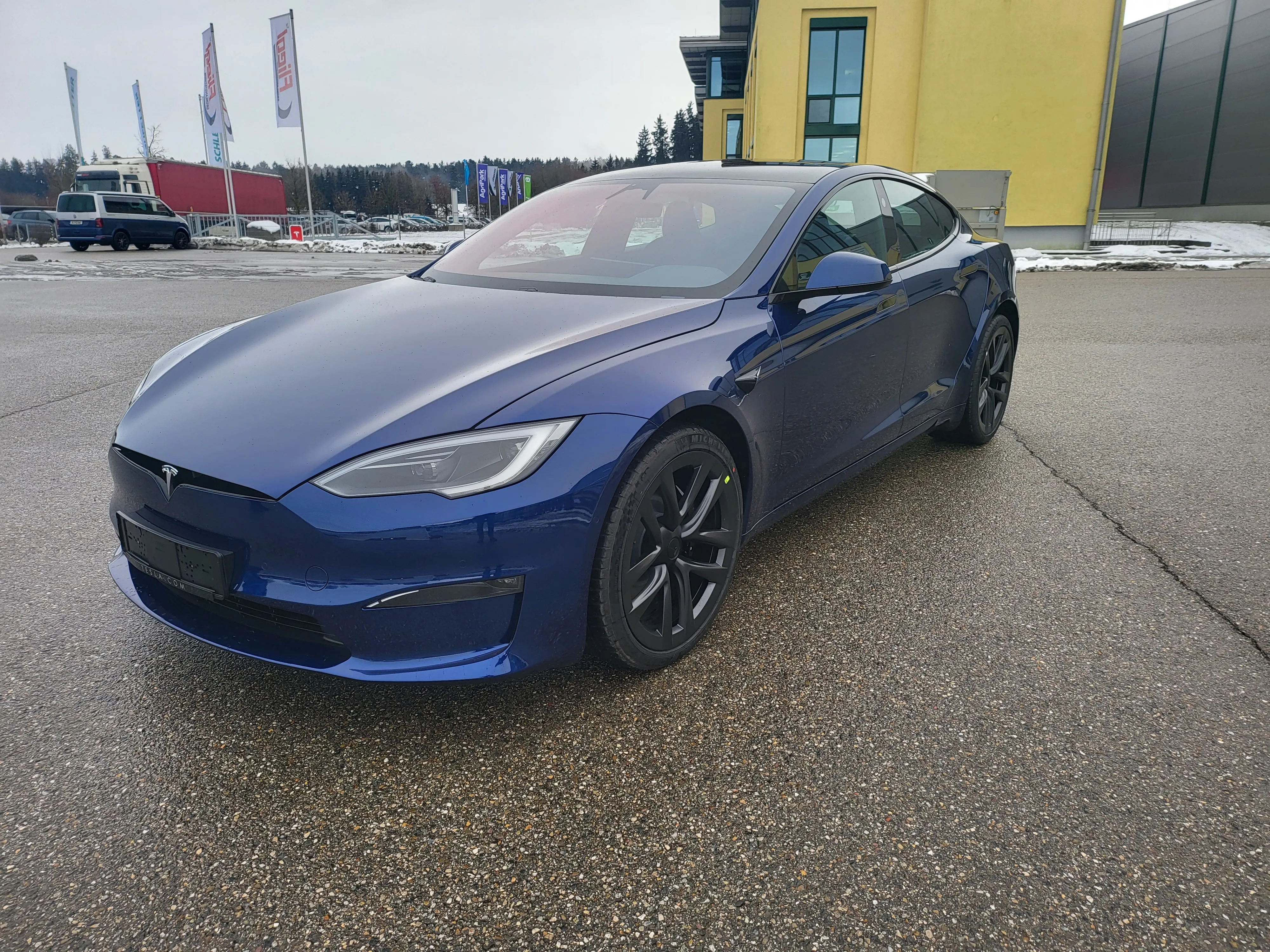 Model S Plaid in Deep Blue schräg von vorne links vor der gelben Halle