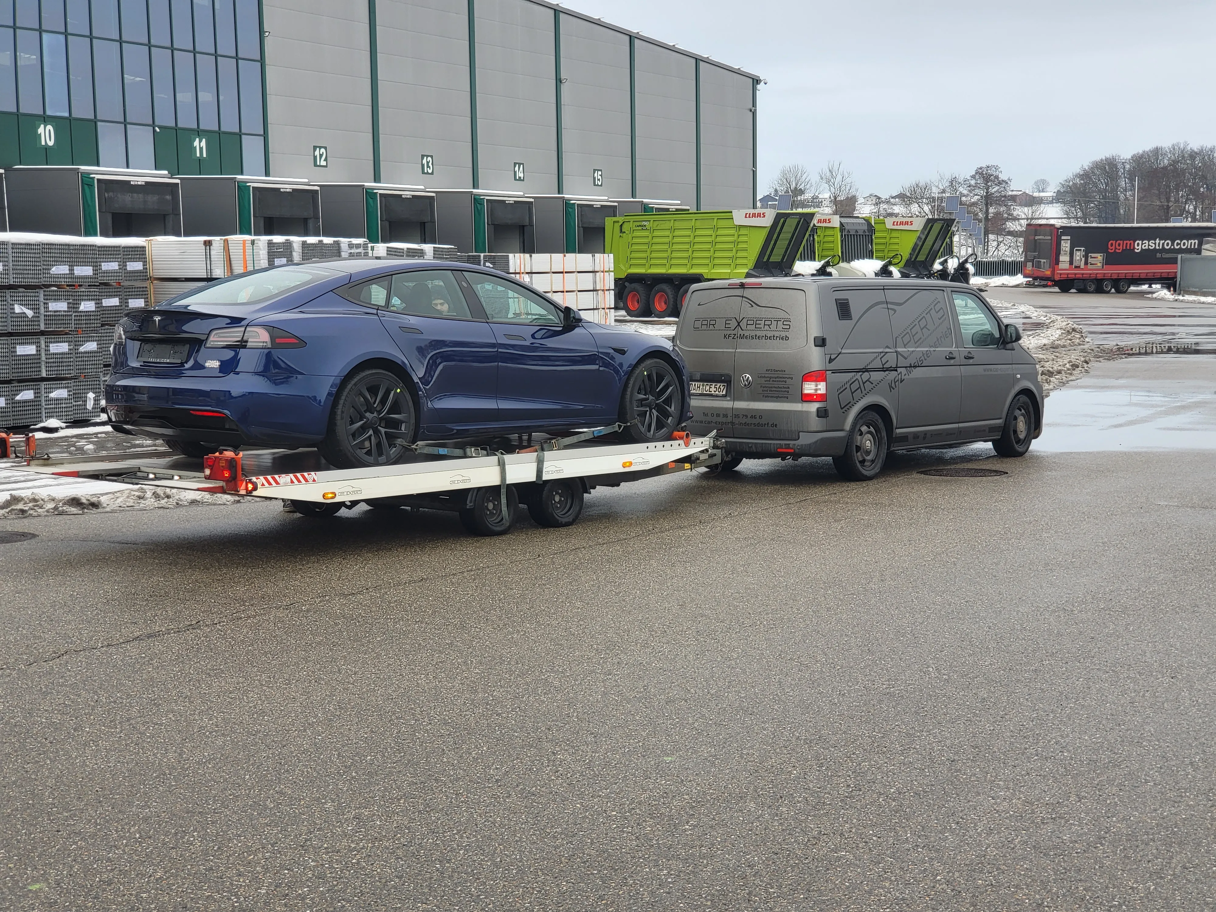 Beladener Autotransporter mit dem blauen Model S vor den Hallen des Gewerbeparks