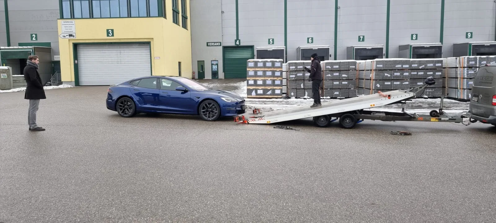 Blick über den Hof: das Fahrzeug auf dem Anhänger, daneben eine wartende Person